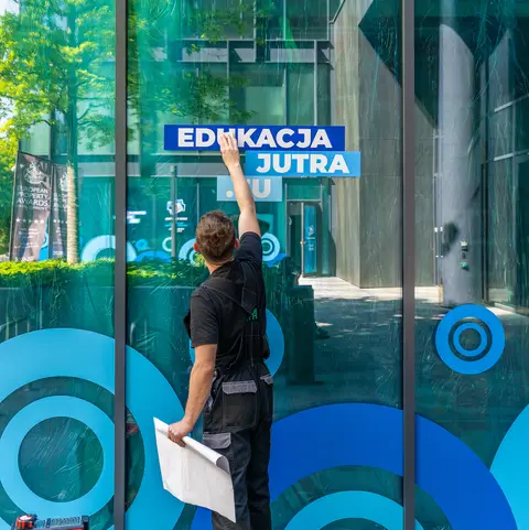 Montażysta nakleja folię z nadrukiem na witrynę